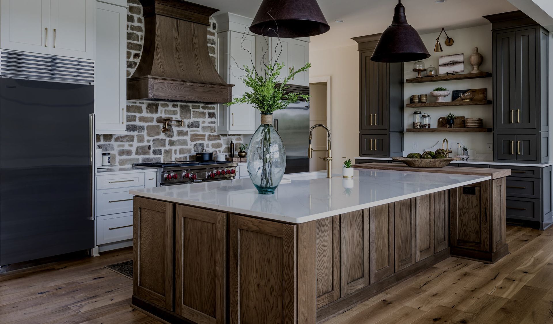 Rustic kitchen with wood cabinets, stone backsplash, island with white countertop, and dark pendant lights.