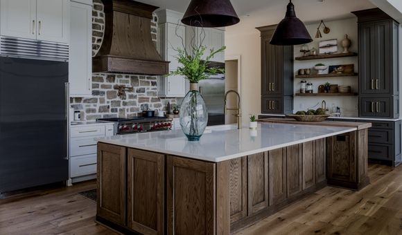 Rustic kitchen with wood cabinets, stone backsplash, island with white countertop, and dark pendant lights.