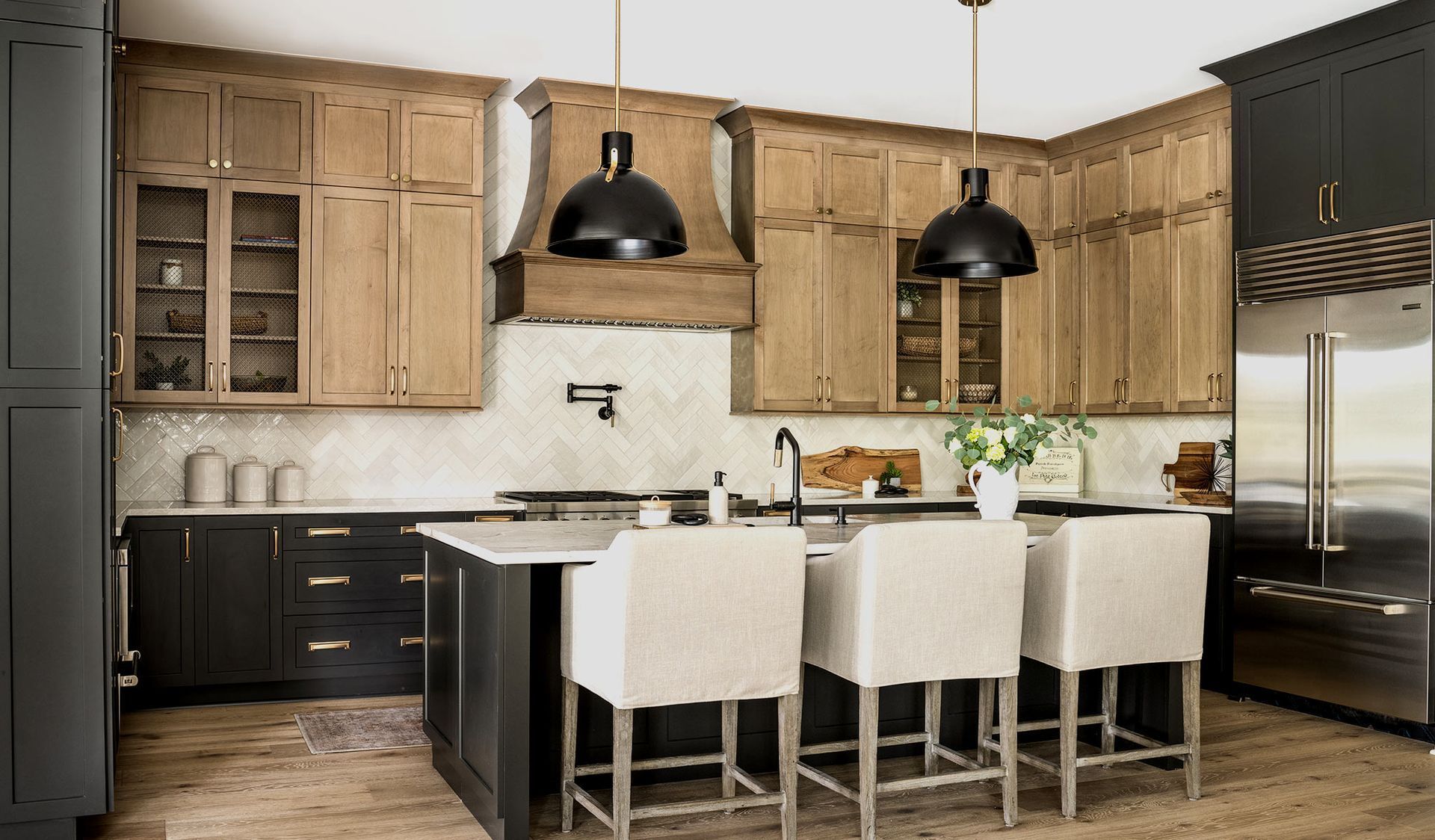 Modern kitchen with dark and light wood cabinets, island with stools, and black pendant lights.