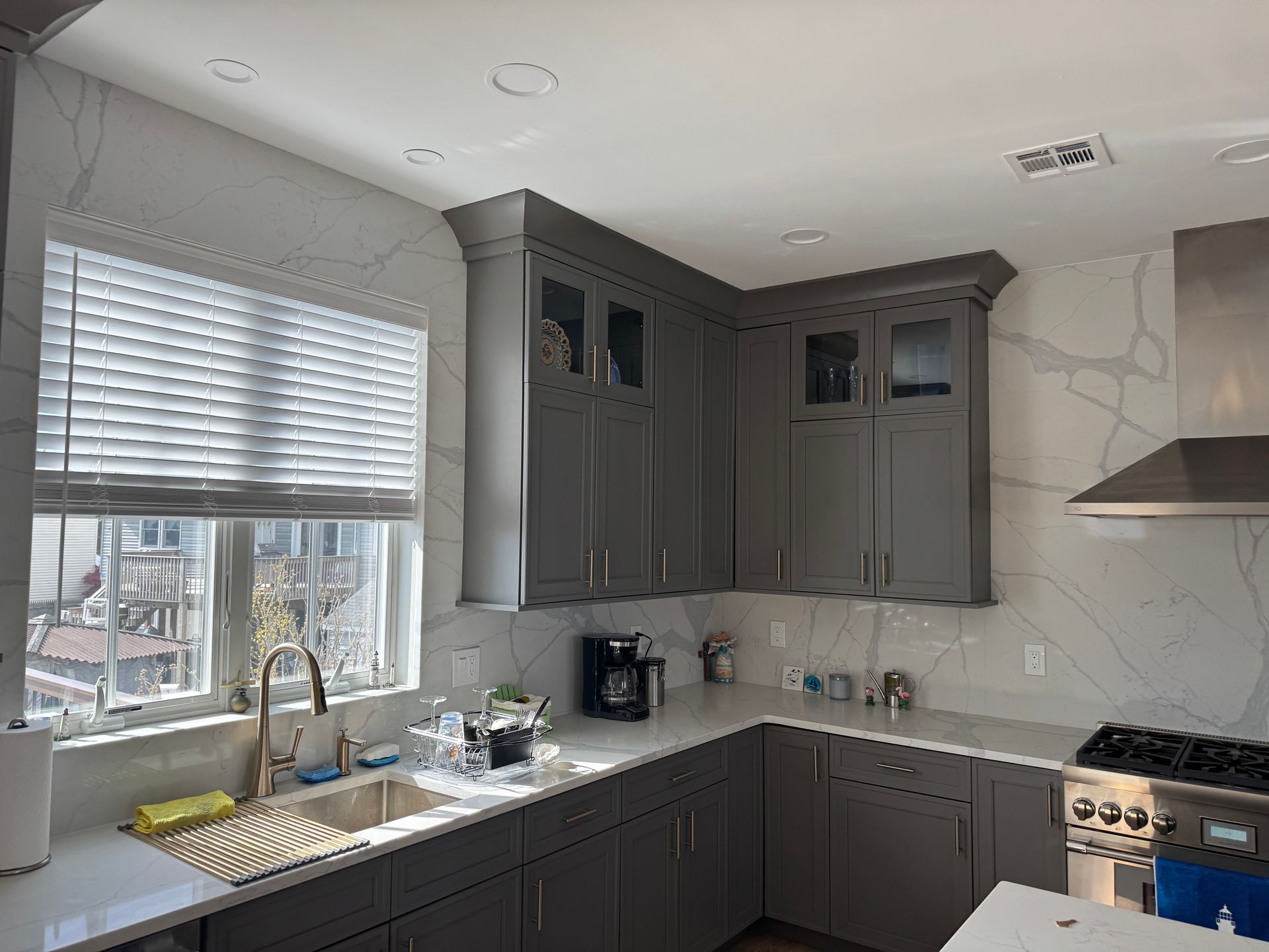 Modern gray kitchen with white tile backsplash, large window, dark cabinets, and stainless steel range hood