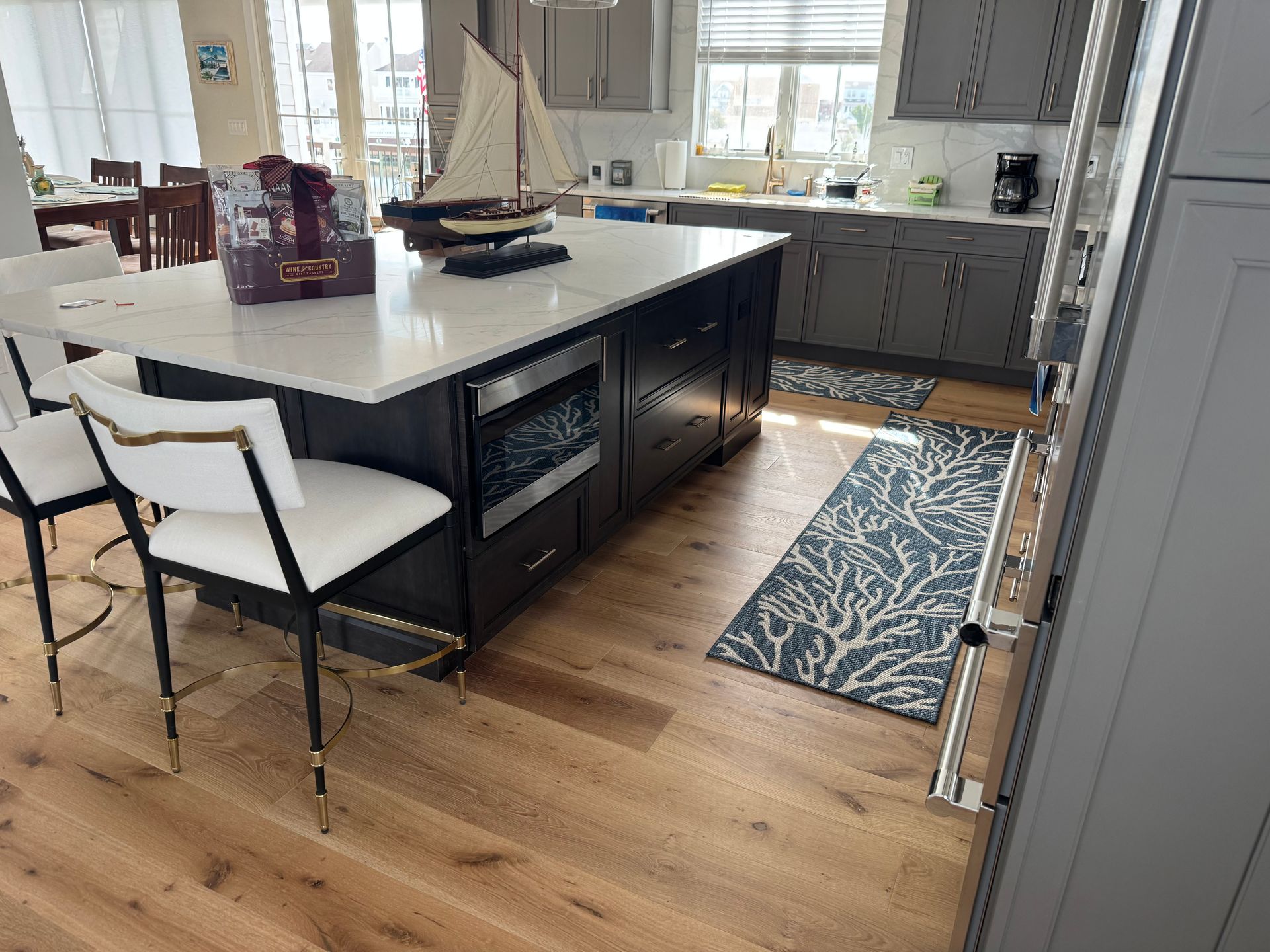 Modern kitchen with a large island, white countertops, black cabinets, and a blue patterned runner on wood floors.