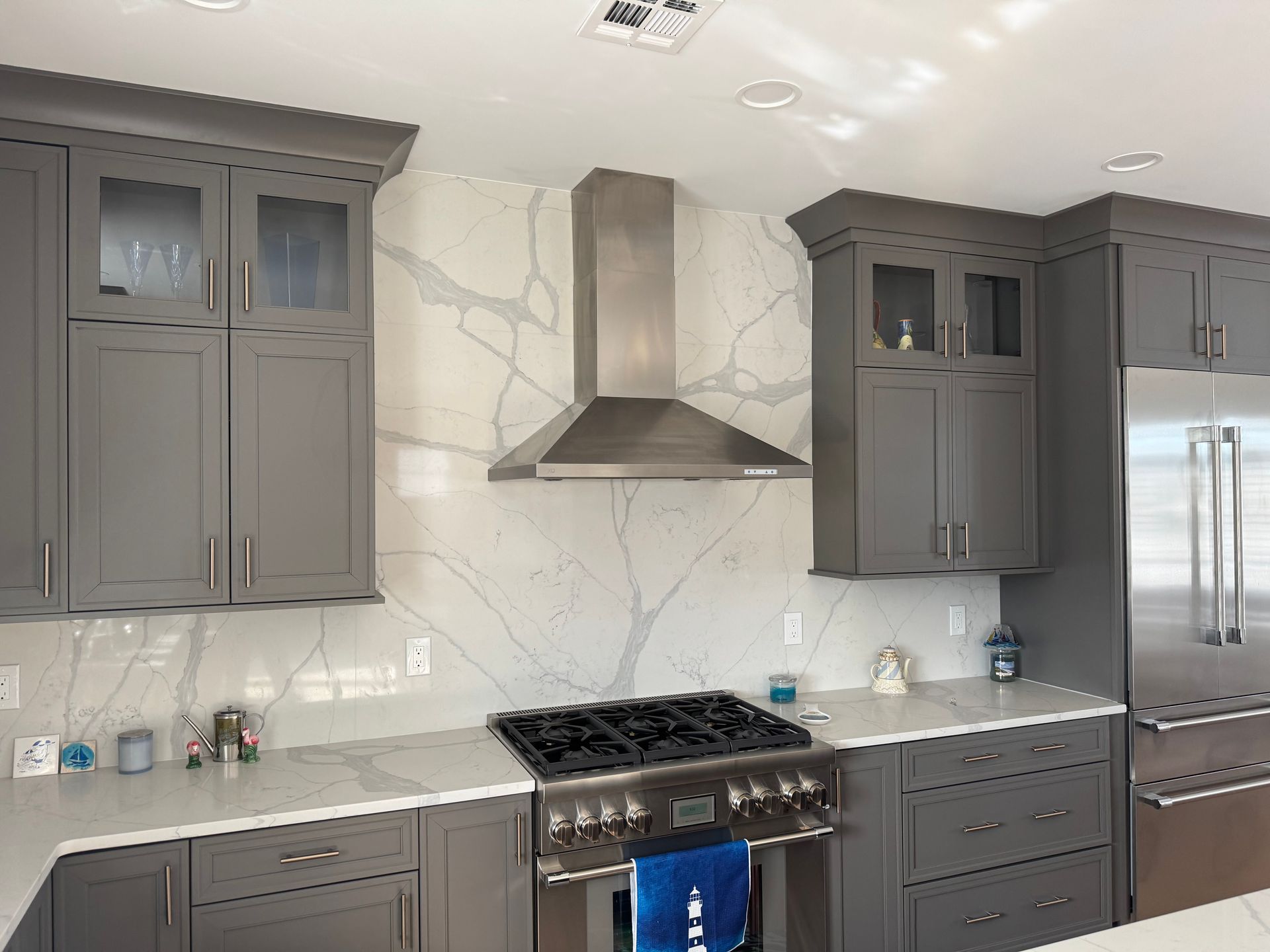 Modern kitchen with gray cabinets, white marble backsplash, stainless steel range hood, and gas stove
