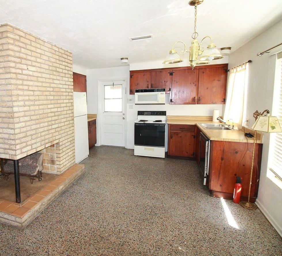 Small kitchen with brick fireplace, wood cabinets, white stove, and a window letting in sunlight.