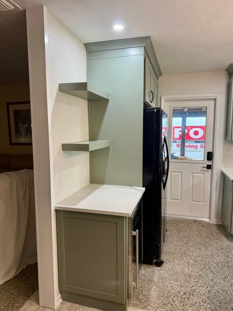 Built-in kitchen nook with white shelves, sage cabinet, and a black coat by the front door.