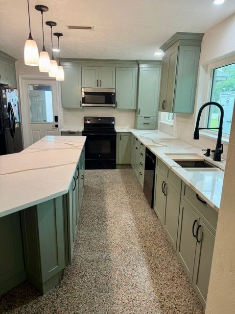 Bright kitchen with sage cabinets, white countertops, black appliances, and a large island.