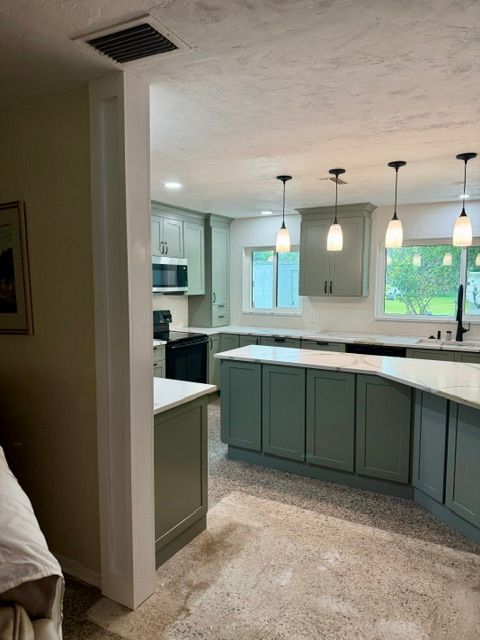 Modern kitchen with teal cabinets, white countertops, pendant lights, and a breakfast bar.