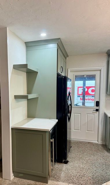 Narrow hallway with built-in storage cabinet, shelves, black fridge, and a back door with frosted glass.