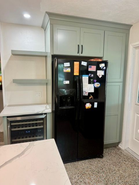 Kitchen with black refrigerator, light green cabinets, open shelves, and a speckled floor.