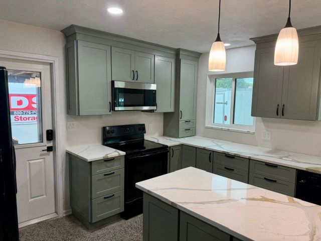 Modern kitchen with sage green cabinets, white countertops, black appliances, and a small island.