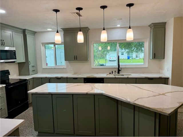 Modern kitchen with sage green cabinets, white countertops, pendant lights, and large windows