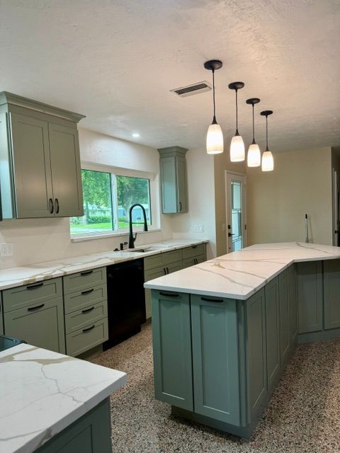 Bright modern kitchen with teal cabinets, marble island, pendant lights, and large window.