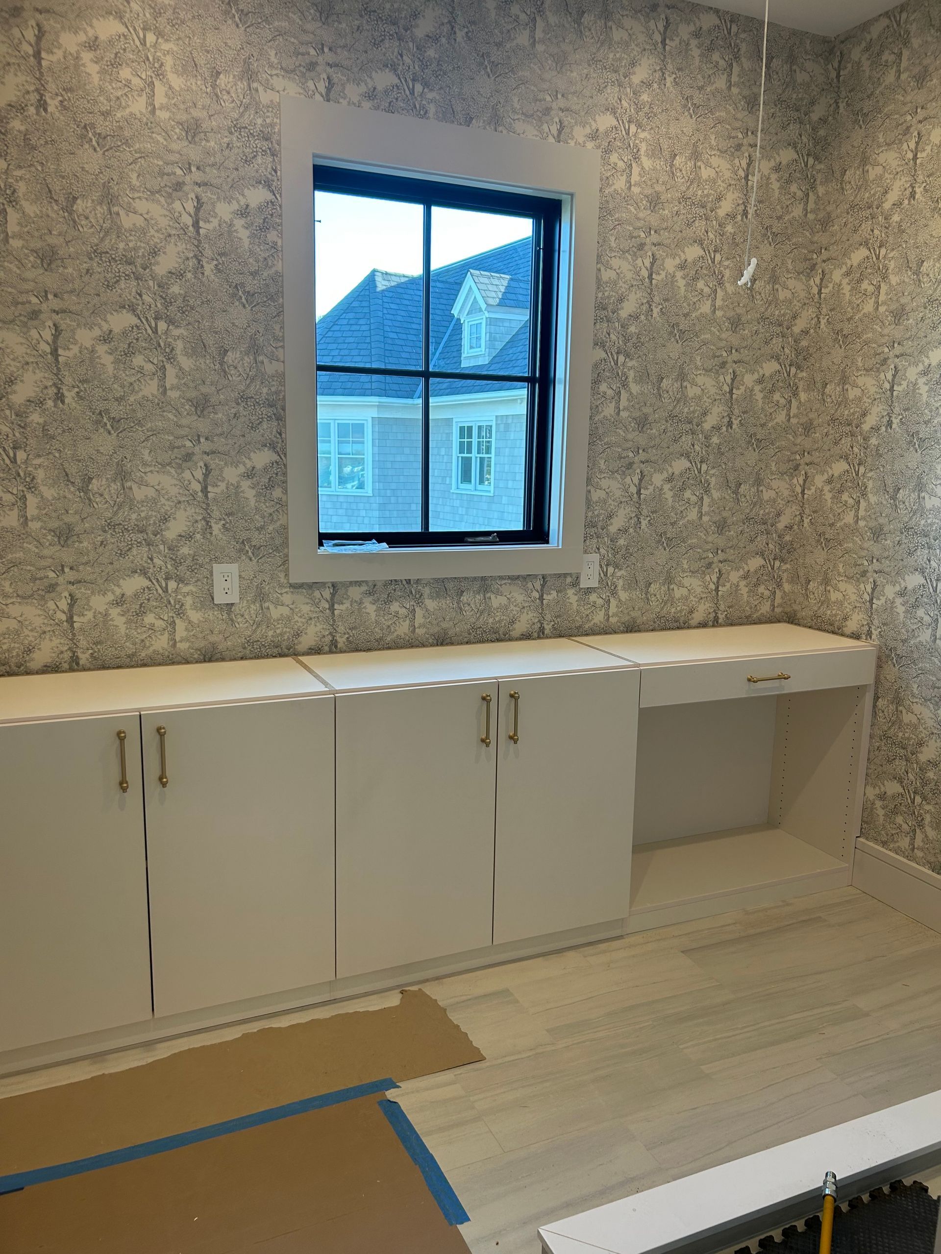 Room with white cabinets, a window, and patterned wallpaper.