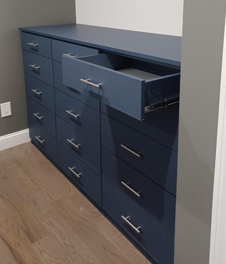 Blue dresser with chrome handles, one drawer open, on a hardwood floor, in a room.