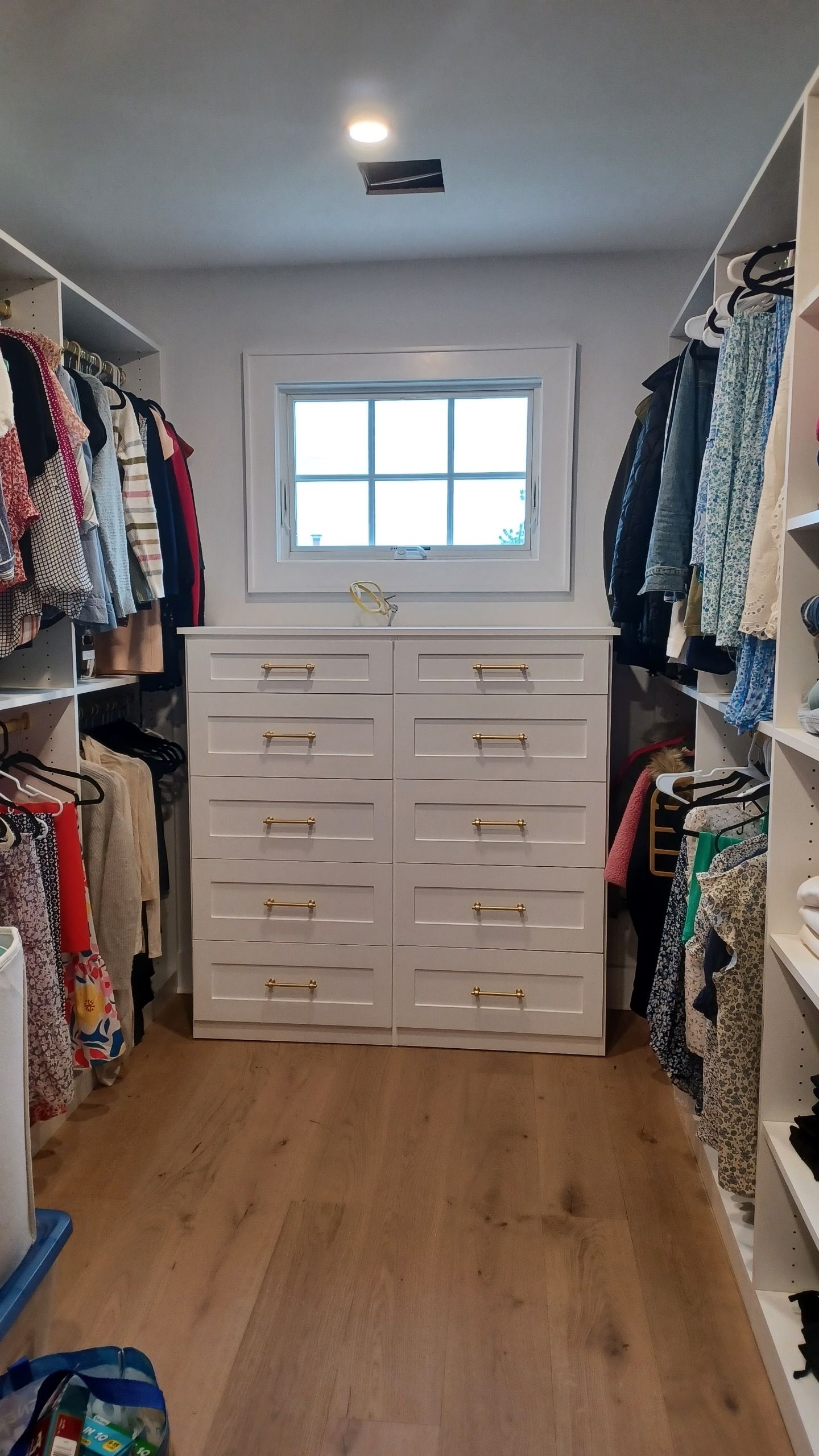 Walk-in closet with white cabinetry, clothes racks, a window, and wooden floor.