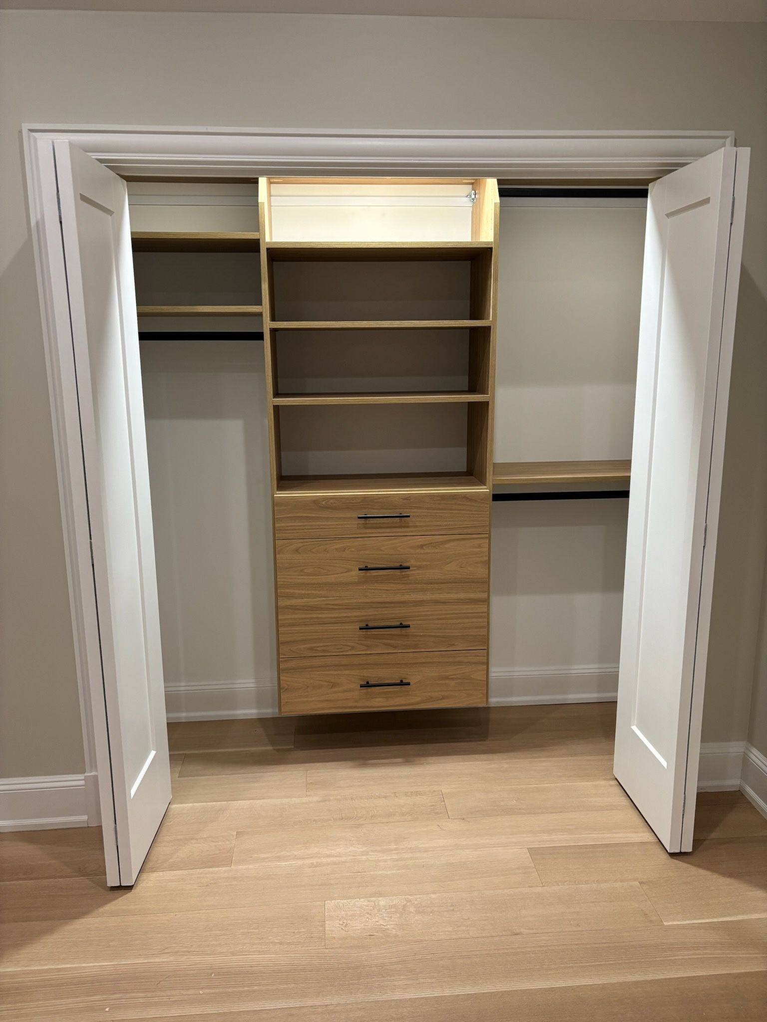 Closet interior with wooden shelving, drawers, and clothes rods, framed by white bi-fold doors.