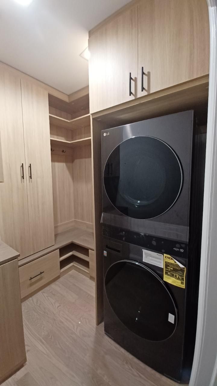Laundry room with stacked black washer and dryer, light wood cabinets and built-in shelving.