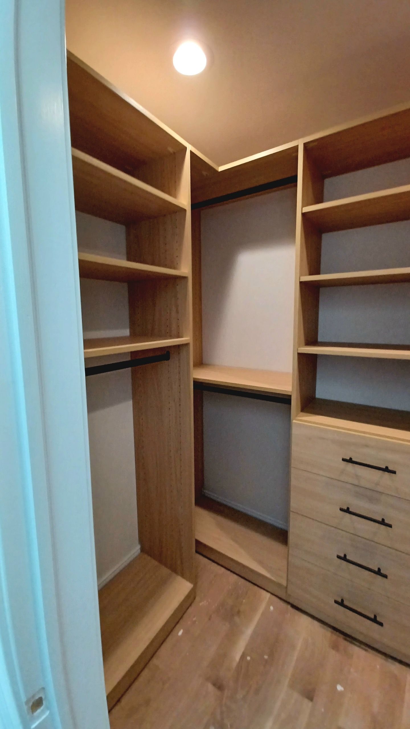 Empty walk-in closet with light wood shelves, drawers, and rods.