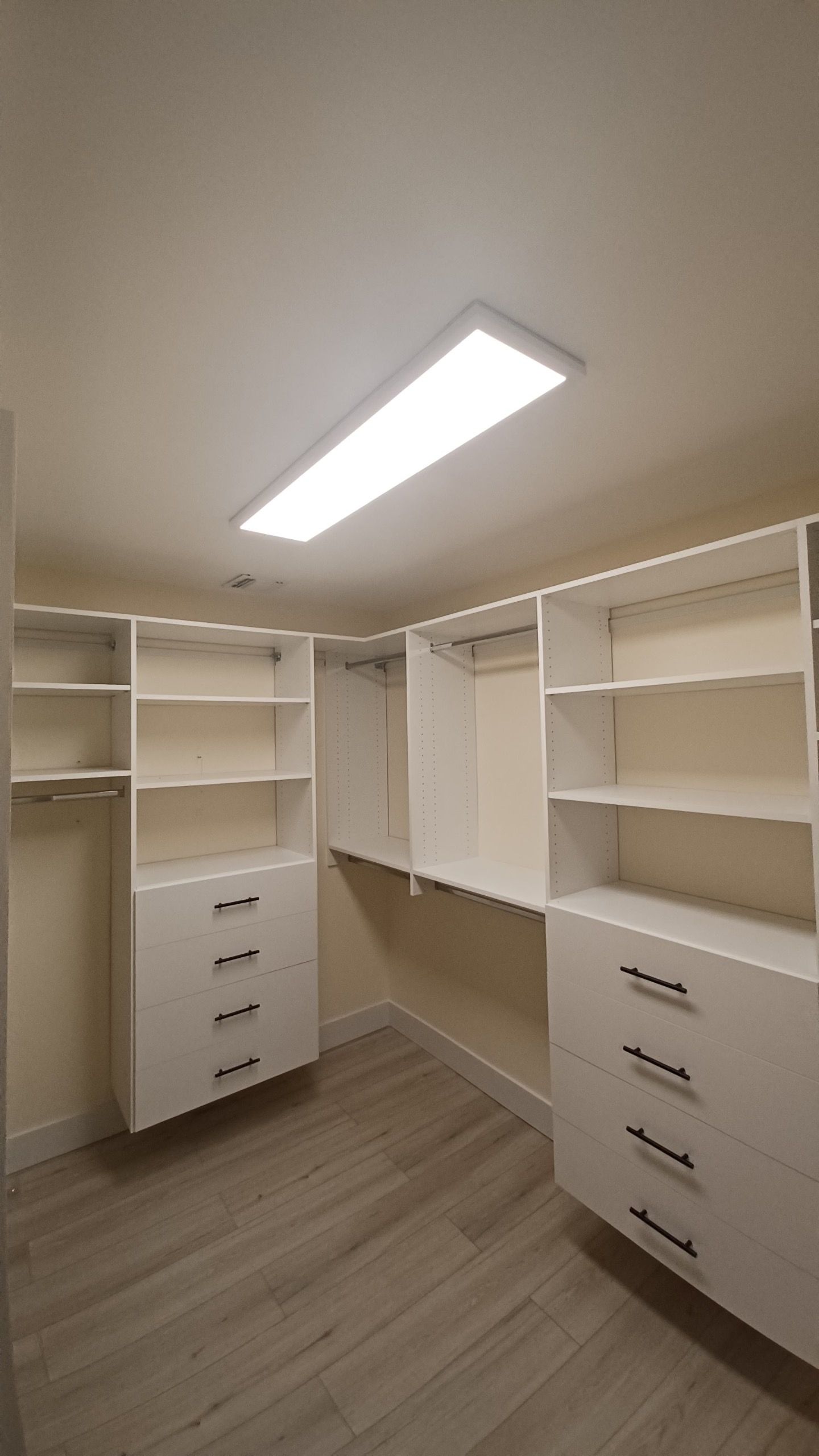 Walk-in closet with white shelves and drawers, a light fixture, and wood-look flooring.