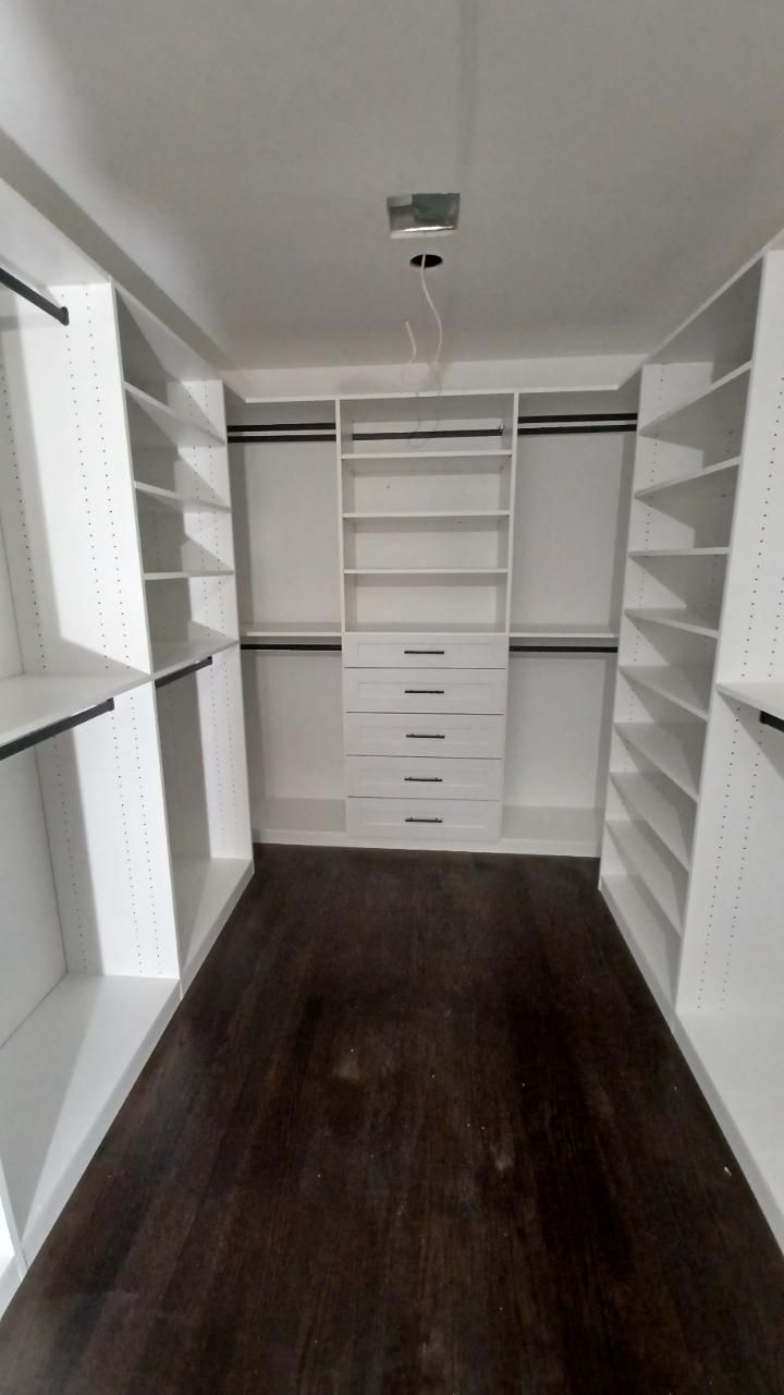 White walk-in closet with shelves, drawers, and hanging rods, dark wood floor, viewed from entrance.