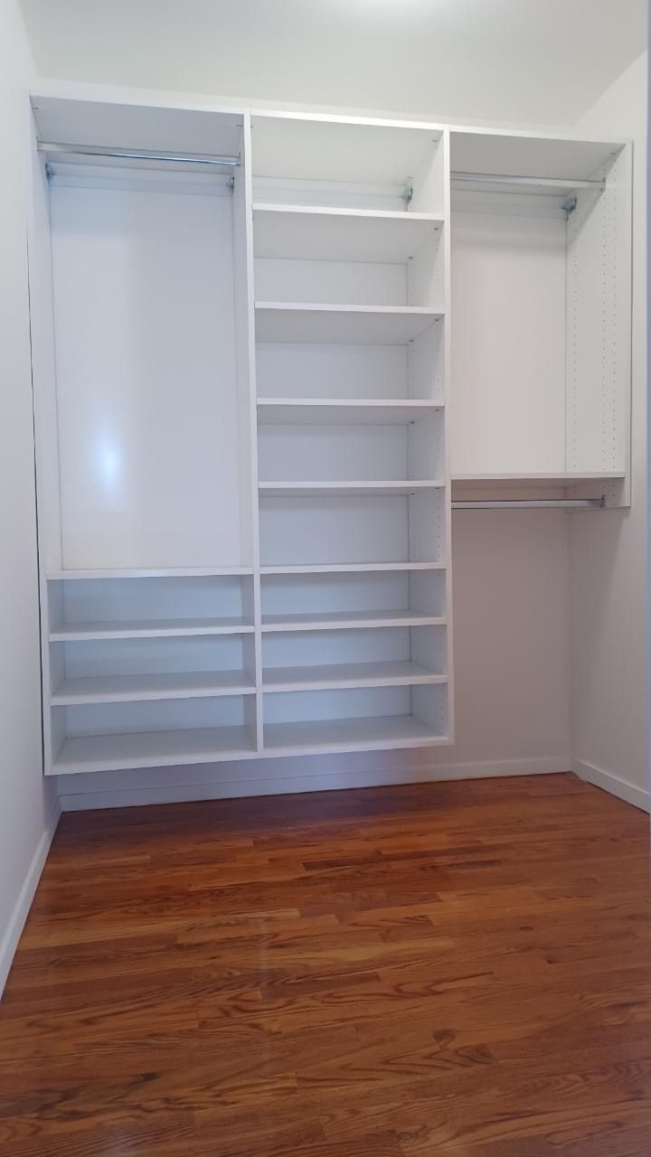 Empty white closet with shelves and hanging rods, set in a room with wooden floors.