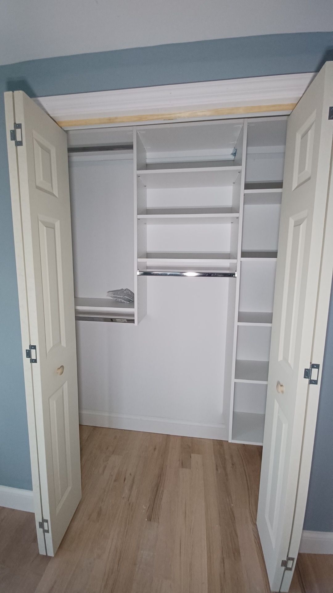 White closet with bi-fold doors open, featuring shelves, rods, and wood-look floor.