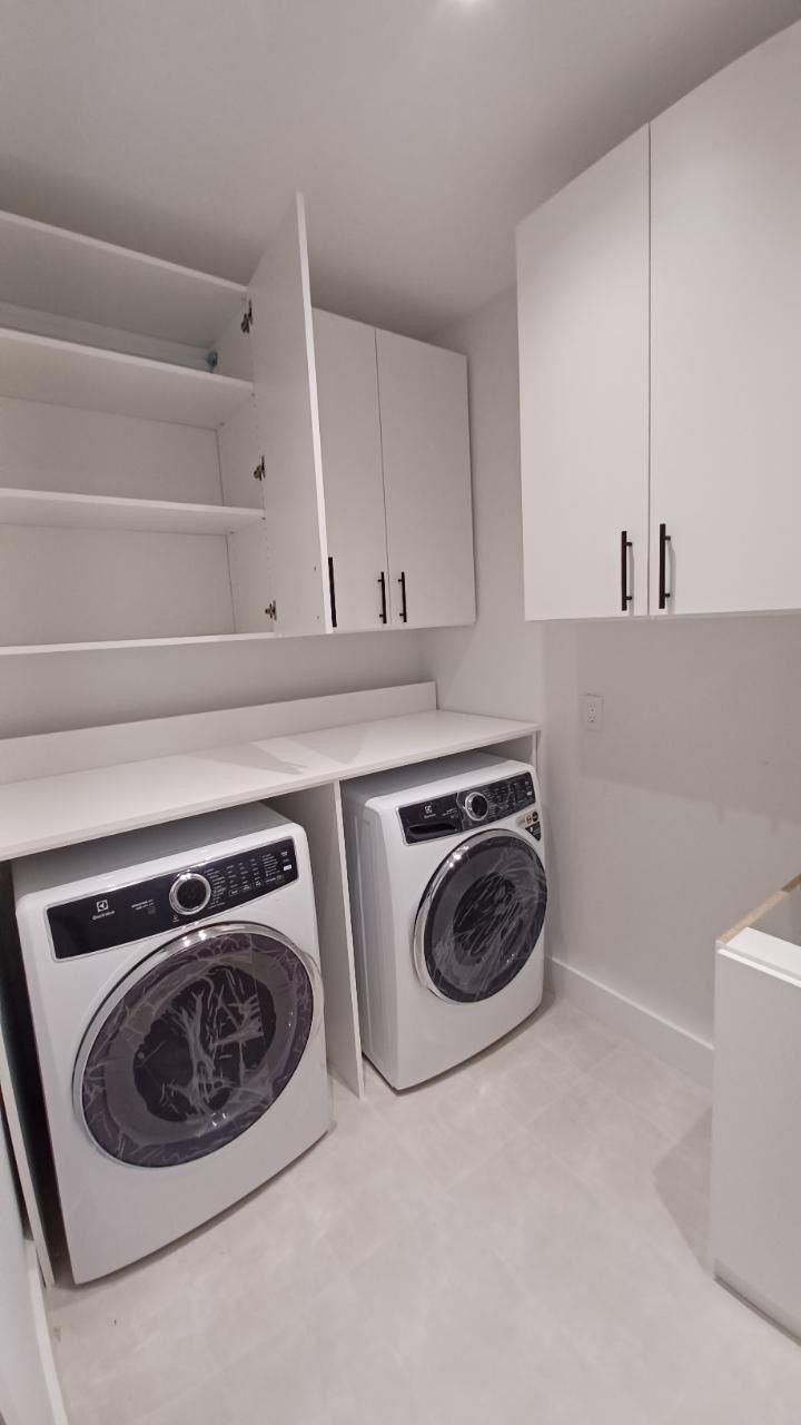 Modern white laundry room with washer, dryer, cabinets, and countertops.