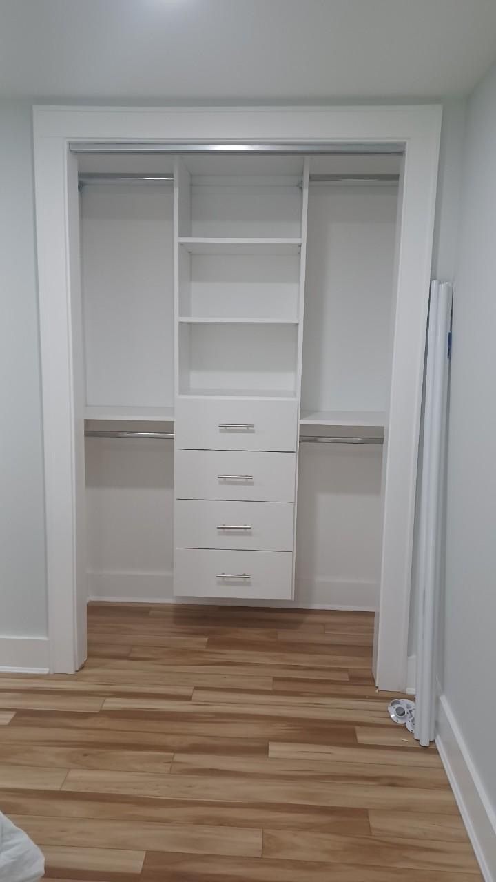 White closet with built-in shelves and drawers in a room with wood-look flooring.