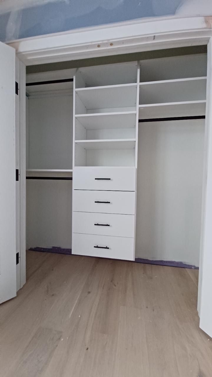White closet interior with shelves, drawers, and hanging rods. Light wood floor.