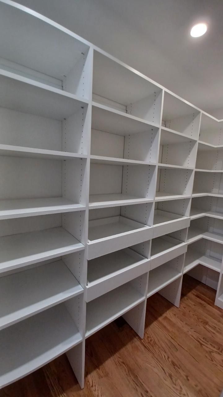 White built-in pantry shelves in a corner, on a wood floor, empty.