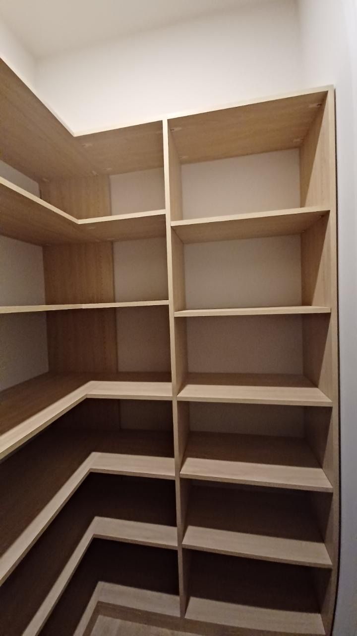 Empty light wood shelves in a pantry. Corner design, against white walls.