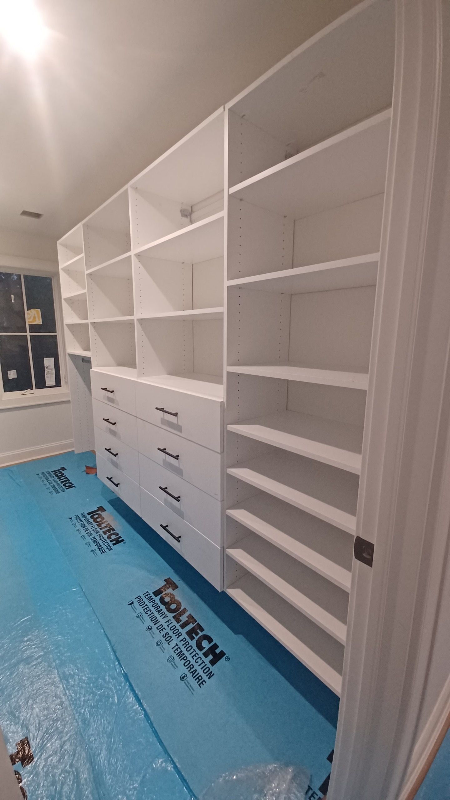 White built-in closet with shelves and drawers; blue protective covering on the floor.