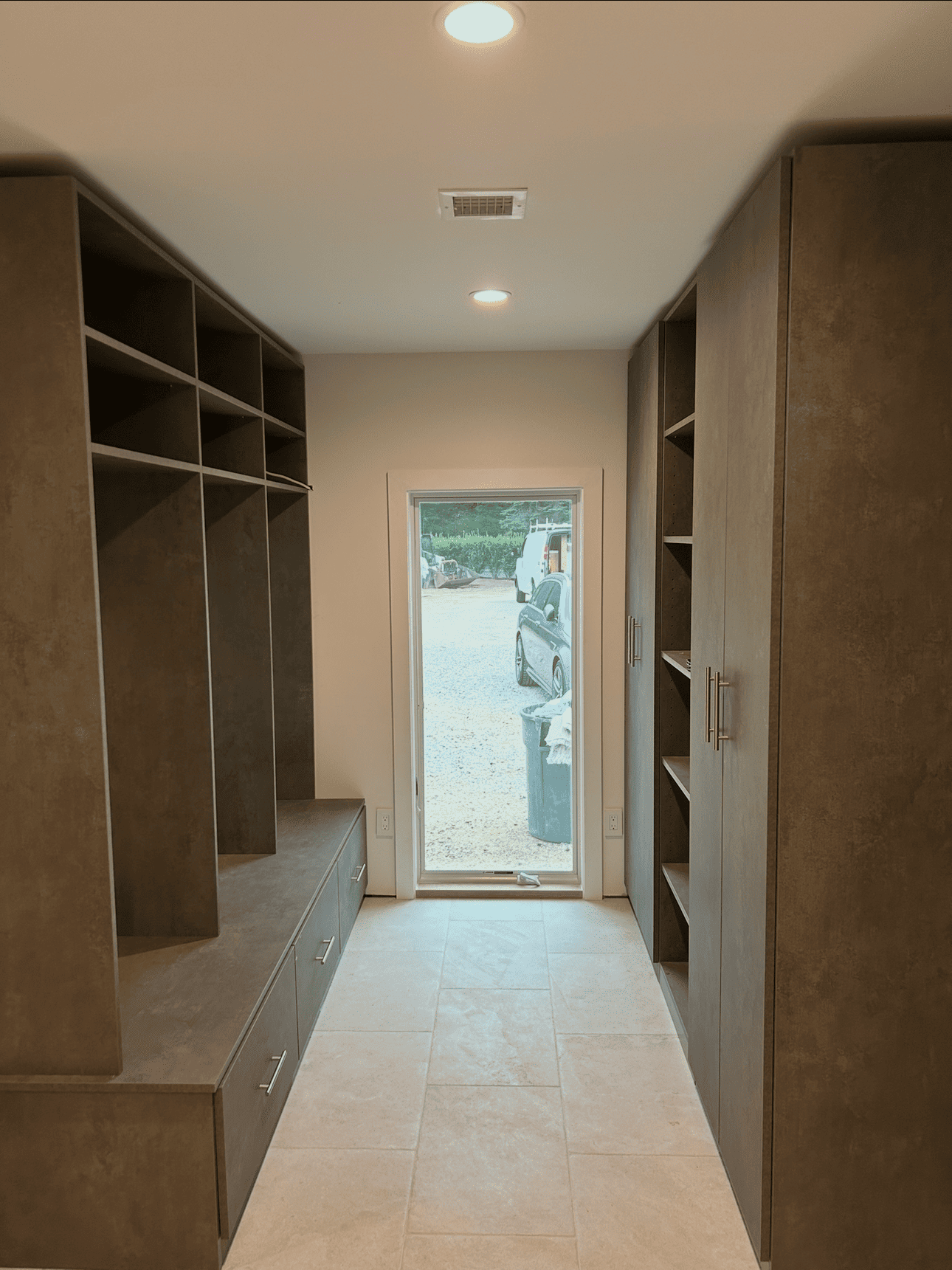 A modern, narrow closet with built-in shelves and storage on either side, leading to a doorway.