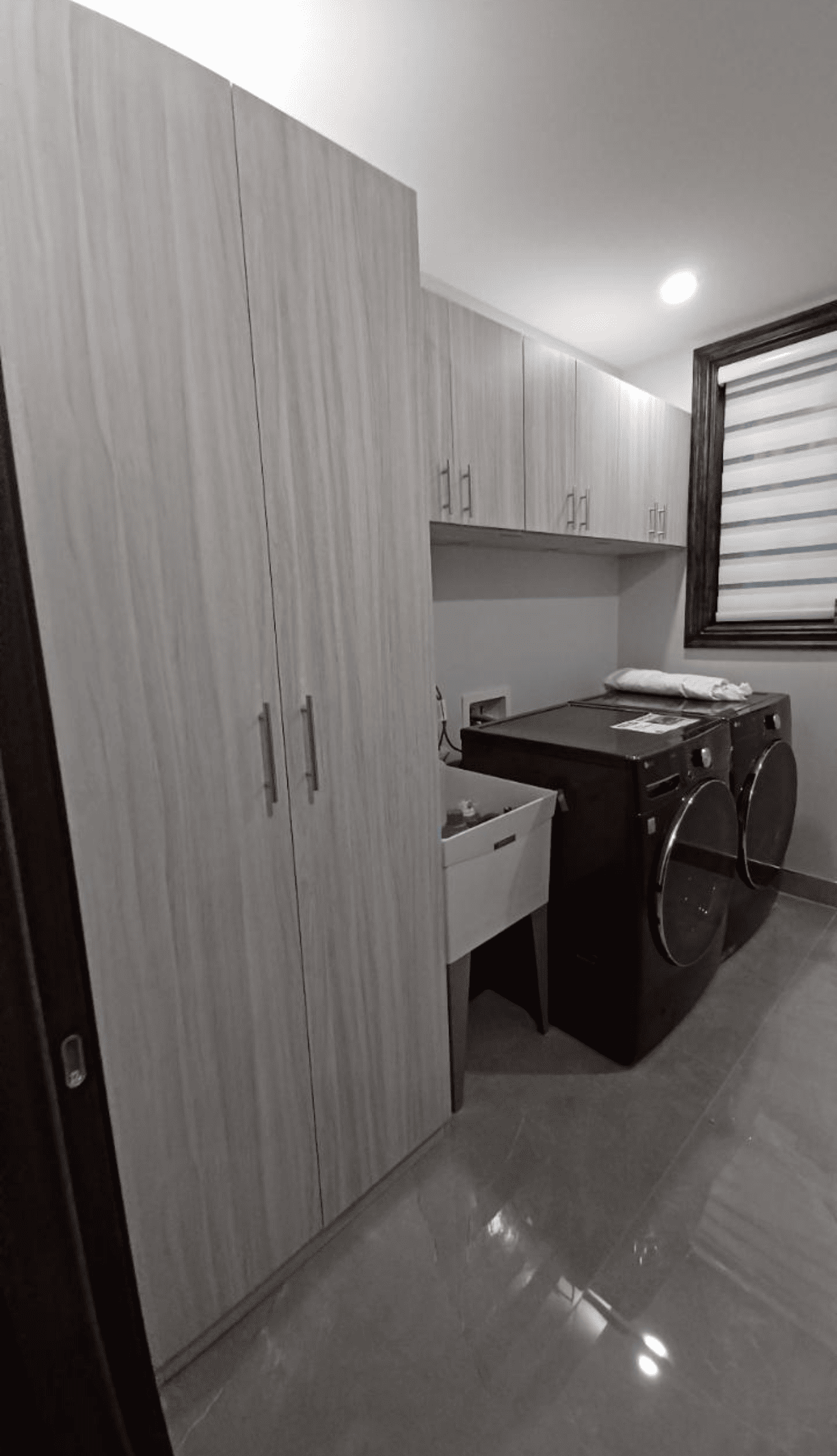 Laundry room with wood cabinets, dark appliances, a sink, and a window.