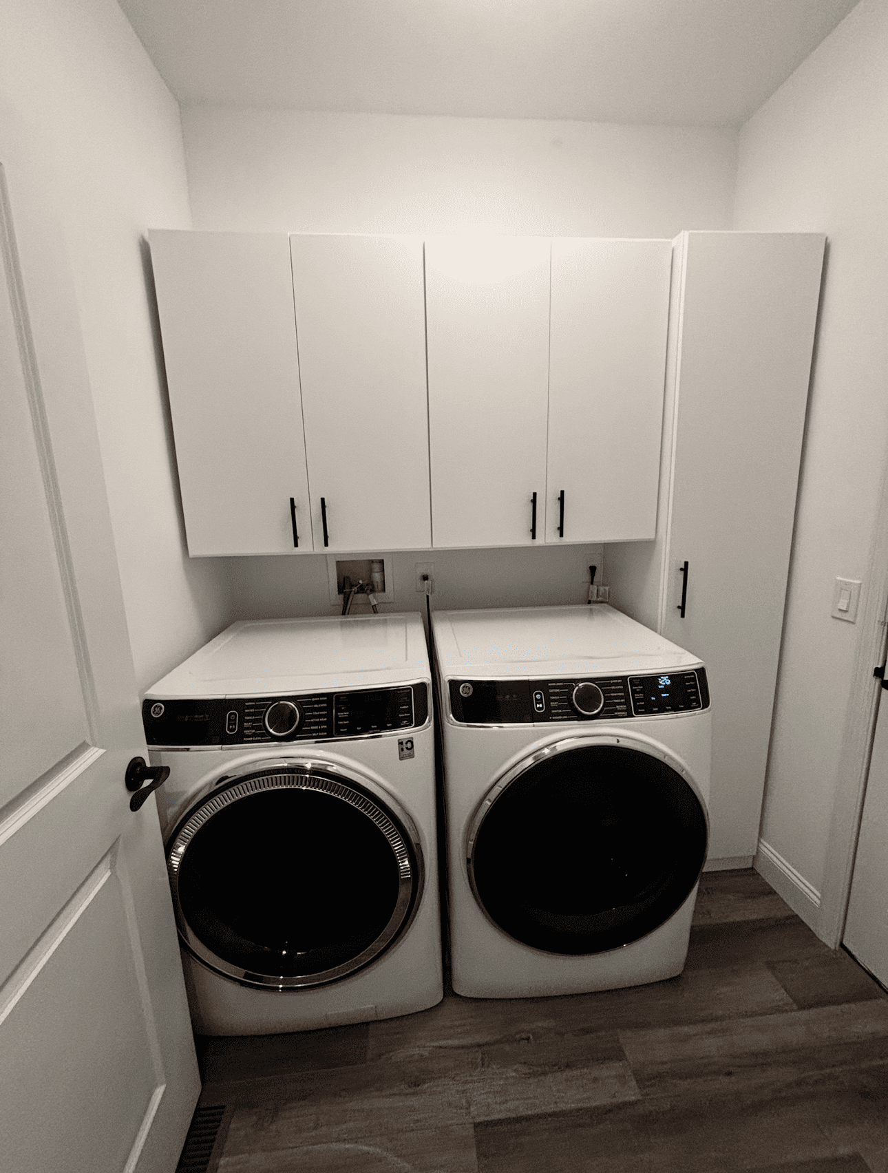 Laundry room with a washer and dryer, white cabinets, and a wooden floor.