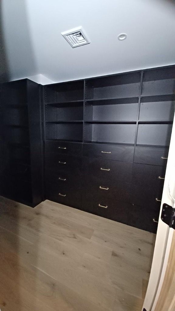 Black closet with shelves and drawers against a light wooden floor.