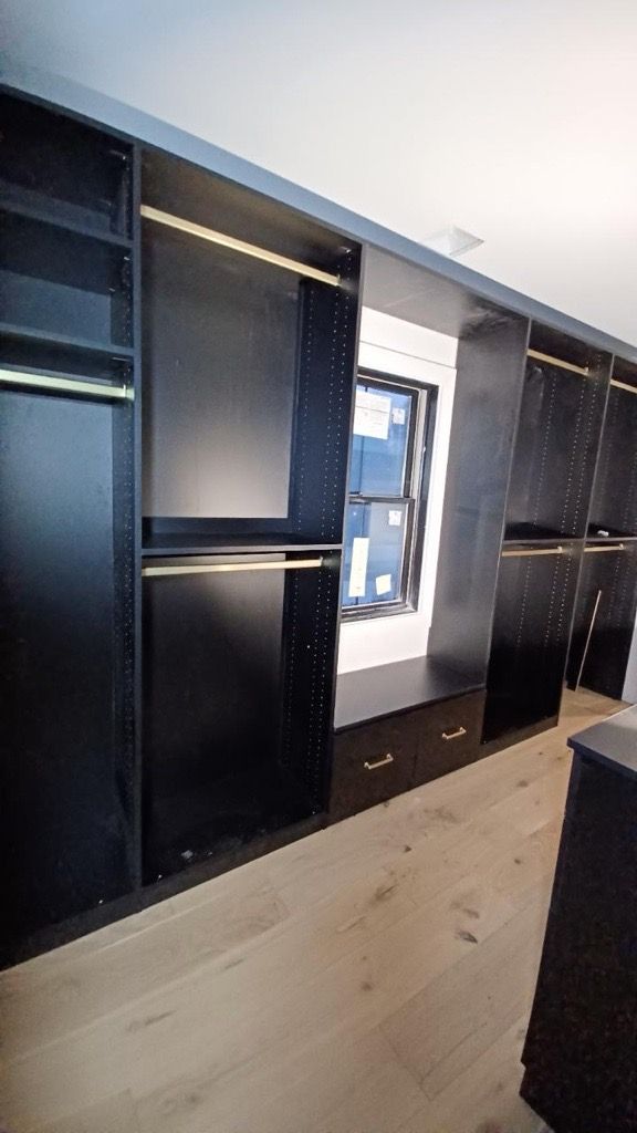 Dark built-in closet with shelves, hanging rods, and a window. Light wood floor and black cabinet doors.