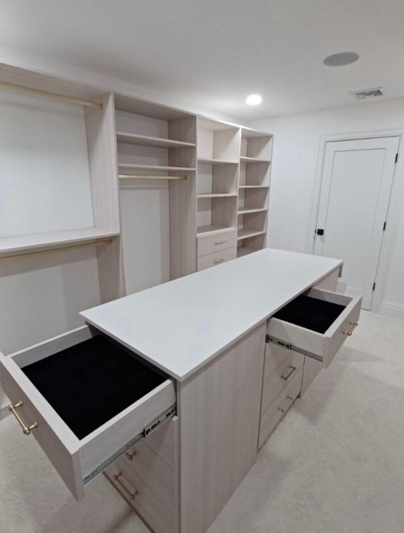 Walk-in closet with light wood shelving, drawers, and an island with open drawers.
