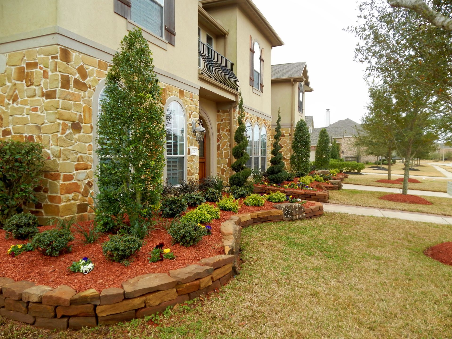 Landscaped front yard with stone flower beds, shrubs, and a beige house exterior