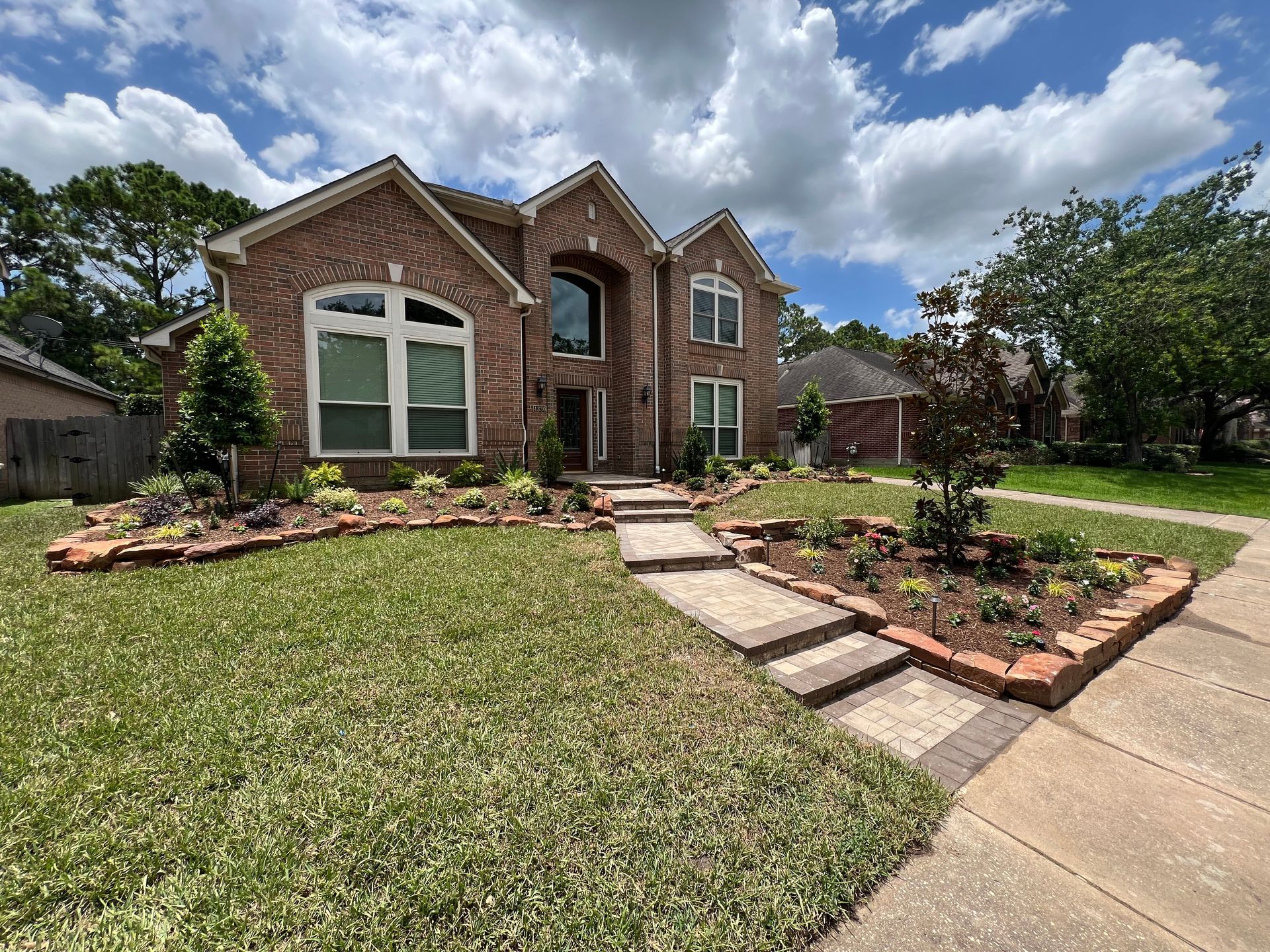 Brick house with arched windows, landscaped front yard, and curved walkway under a cloudy sky