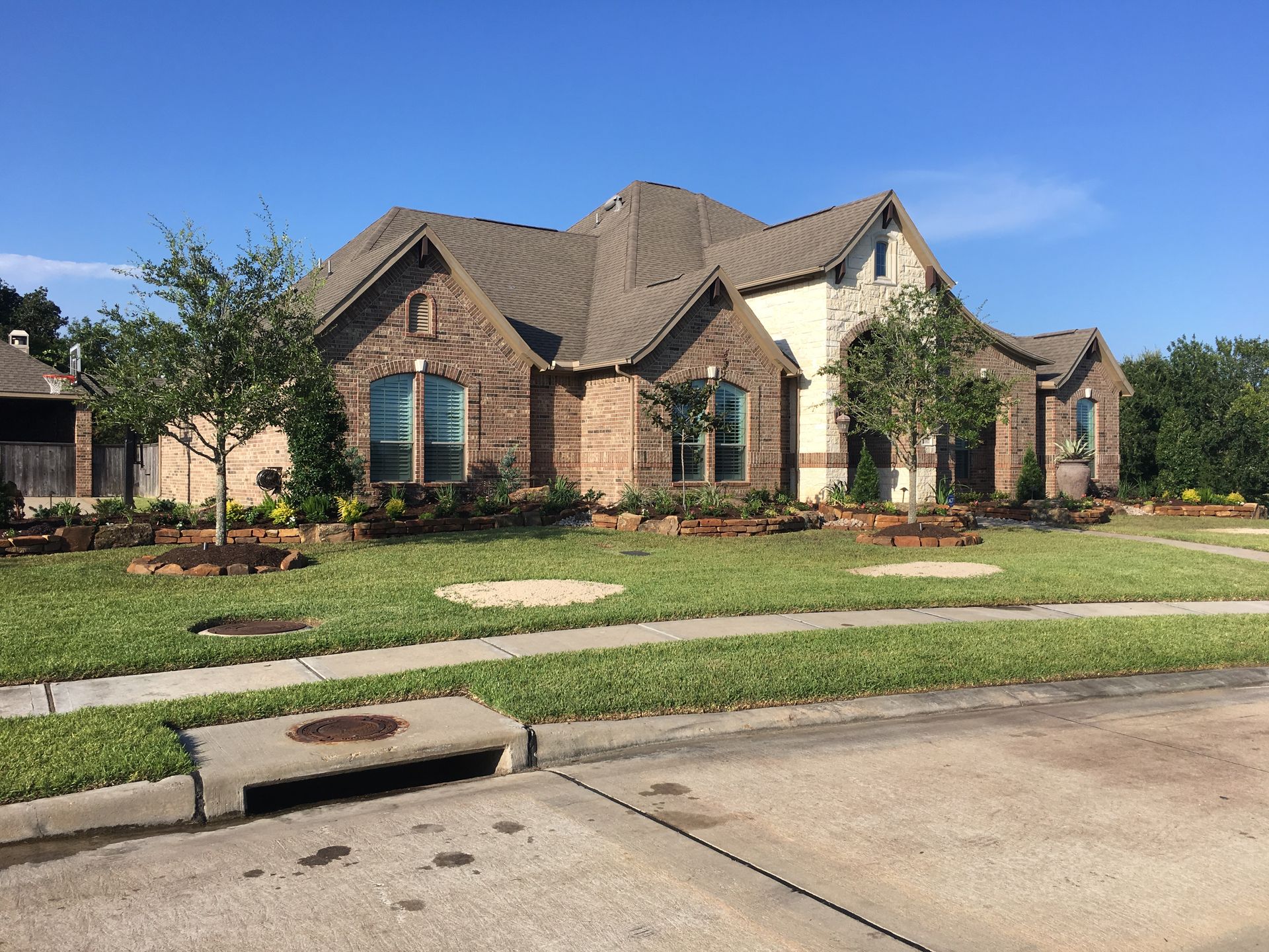 Suburban brick house with a manicured front lawn and clear blue sky