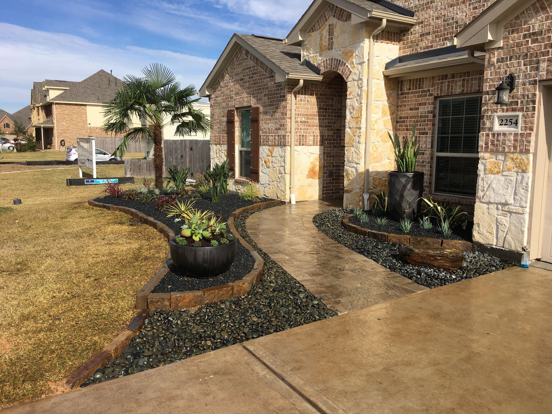 Suburban home front entry with stone walkway, dark mulch beds, and wet driveway after rain