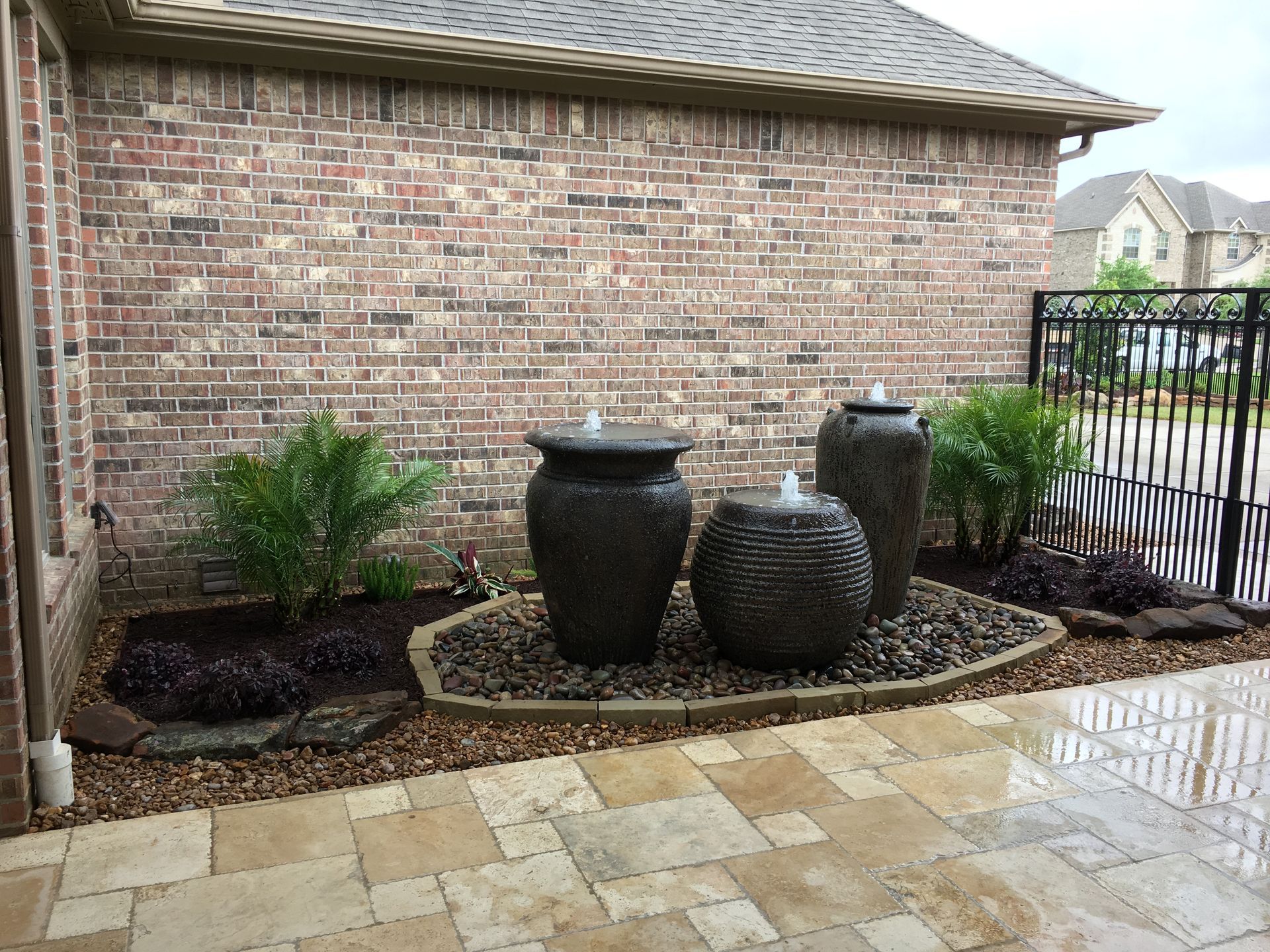 Brick house side yard with decorative black urns, shrubs, and wet stone pavers.
