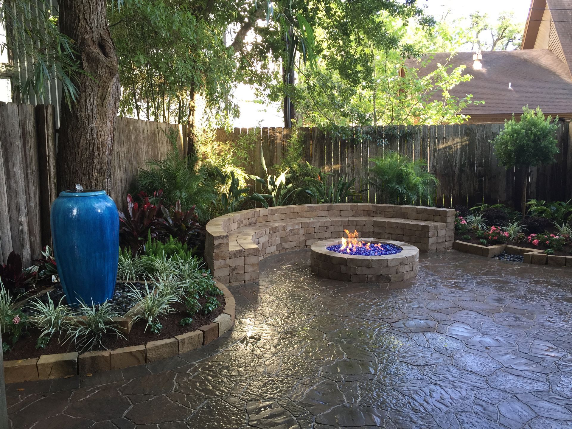 Backyard patio with stone fire pit, curved bench, blue ceramic pot, and lush garden greenery