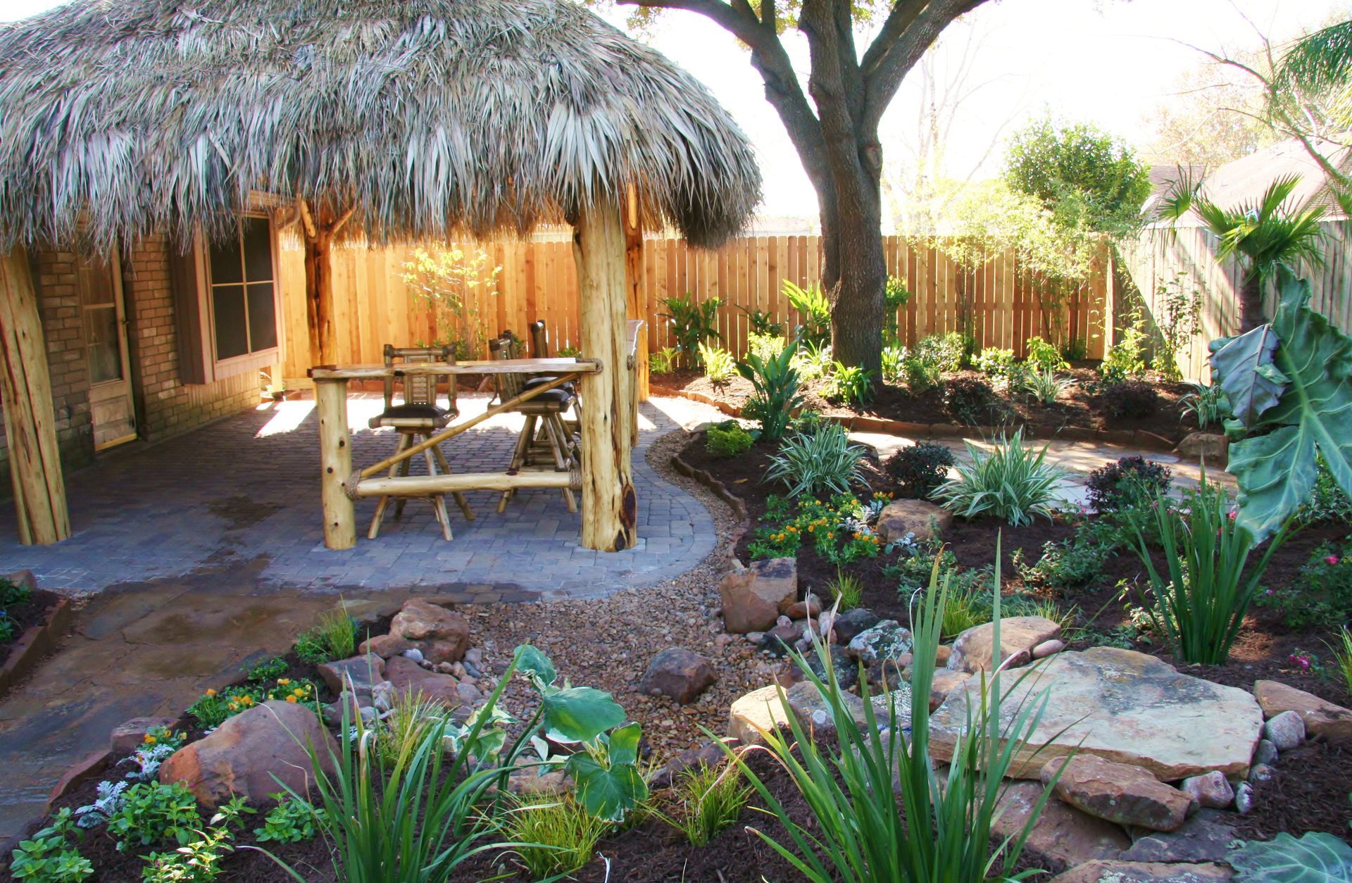 Tropical patio with thatched-roof hut, picnic table, and lush garden plants around a stone path