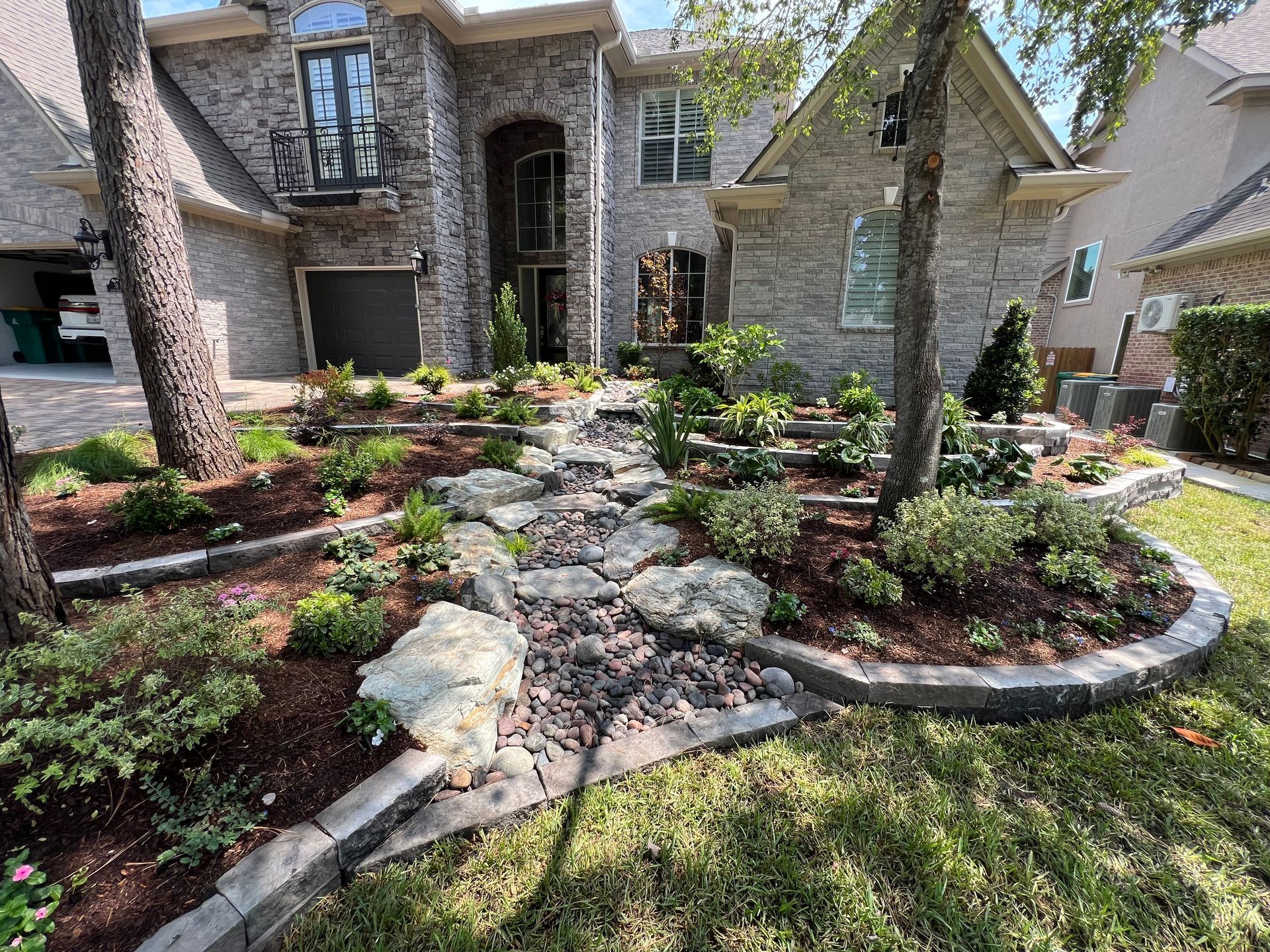 Stone-front house with landscaped front yard, curved flower beds, and a rock-lined walkway