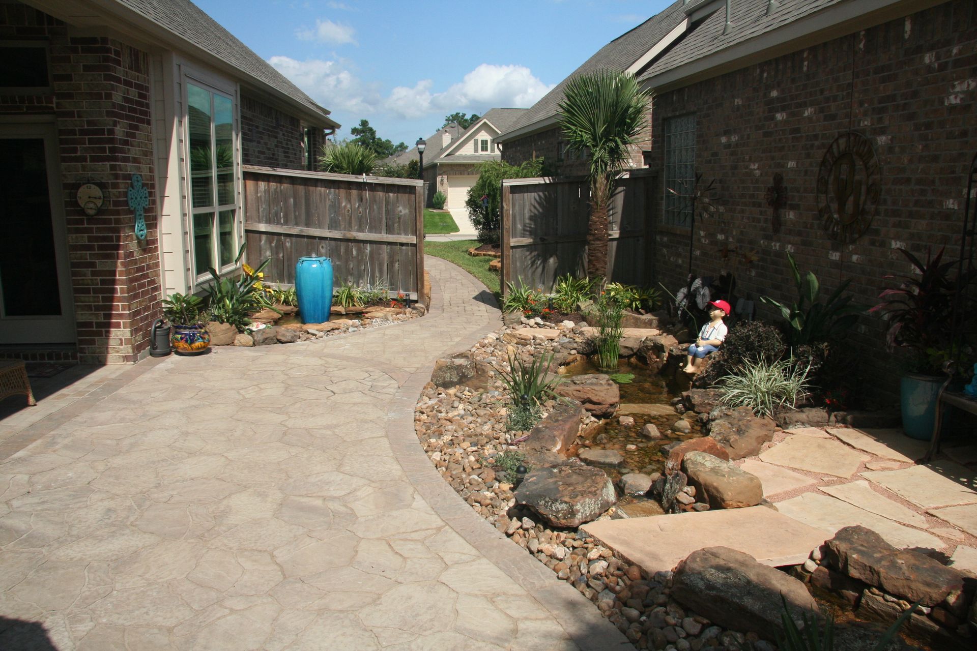 Backyard courtyard with stone path, brick walls, and a small pond garden.