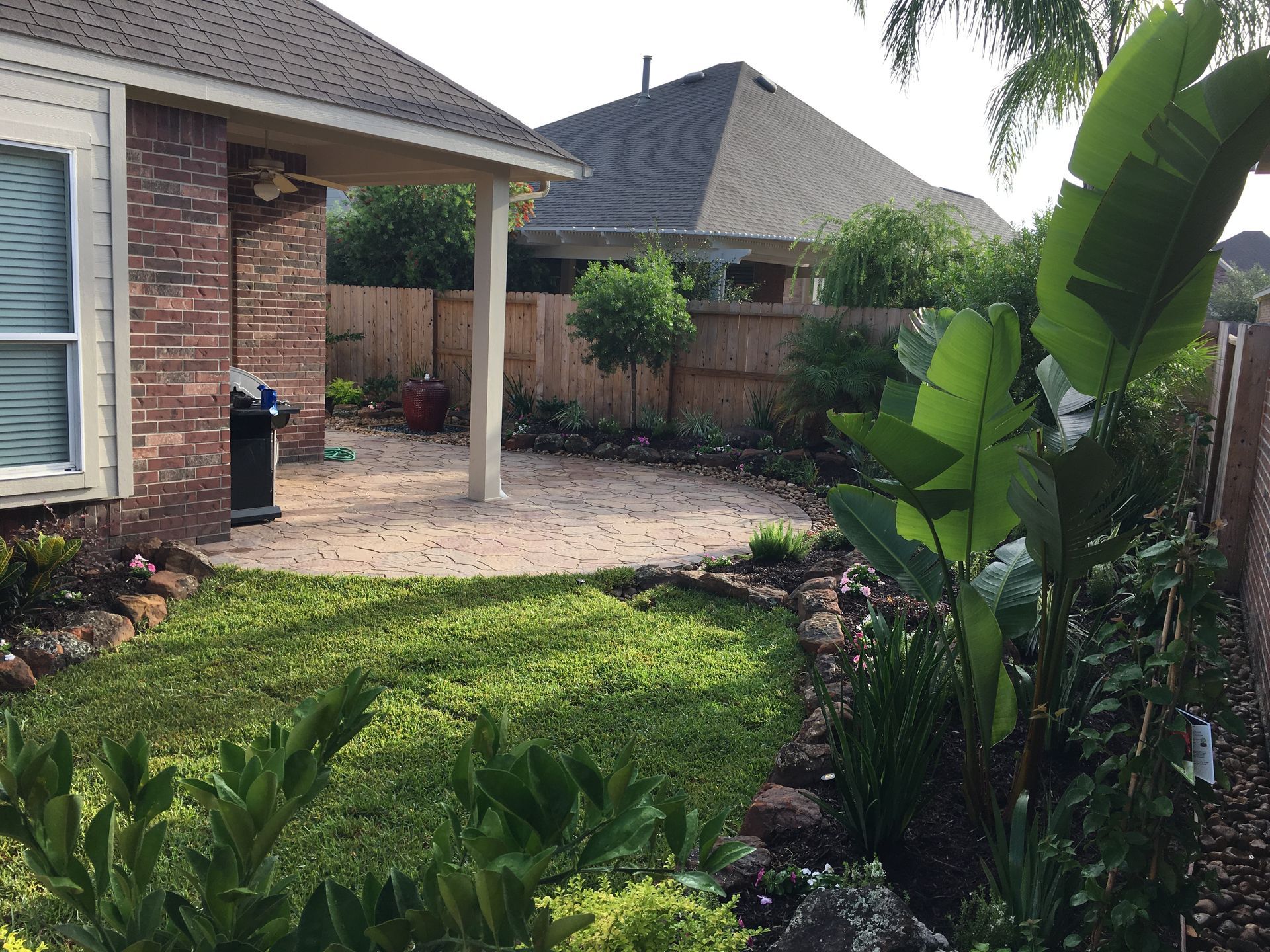 Backyard patio with brick house, paved area, and lush green garden plants