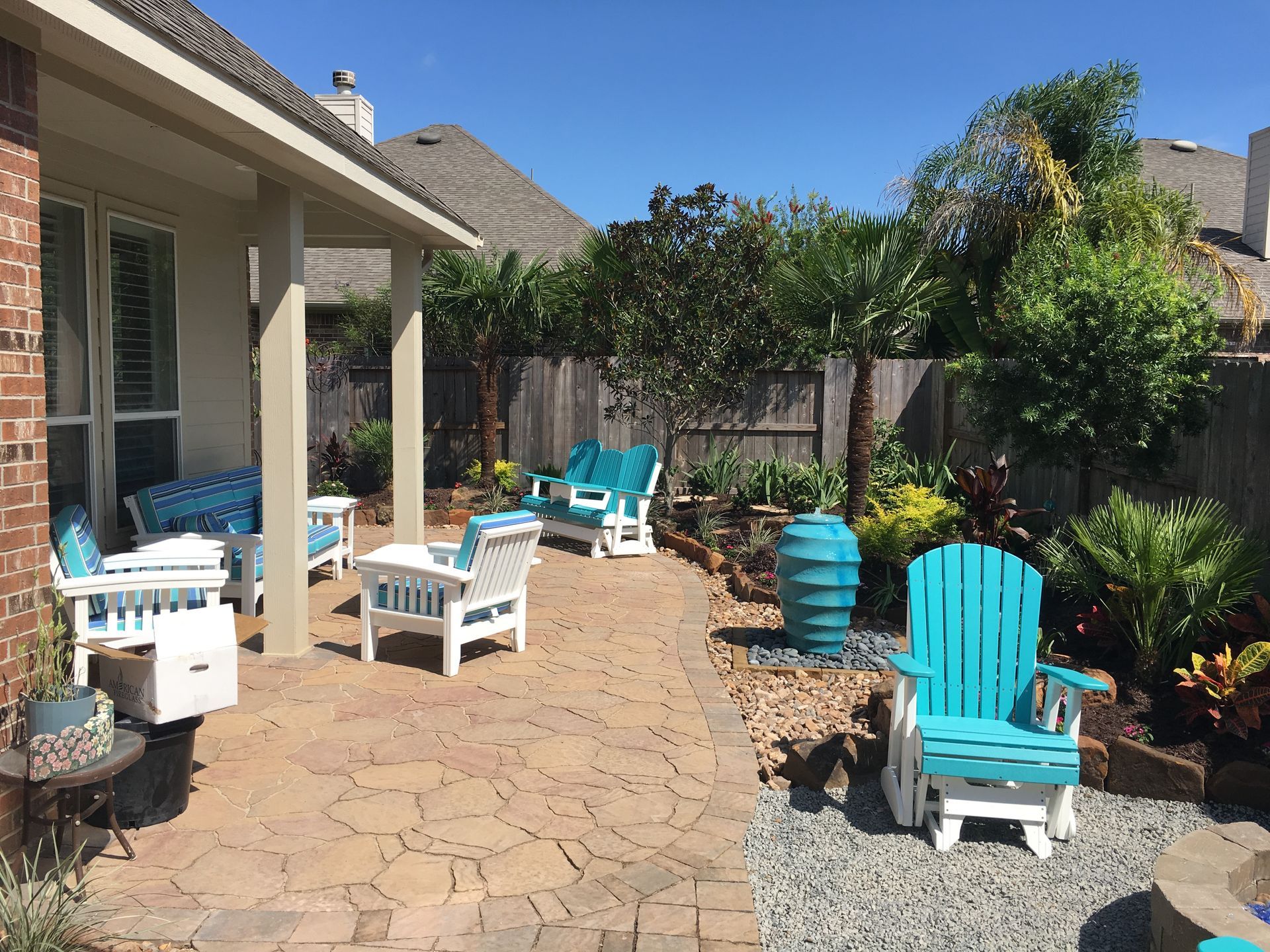 Backyard patio with turquoise chairs, white tables, and potted plants in bright sunlight