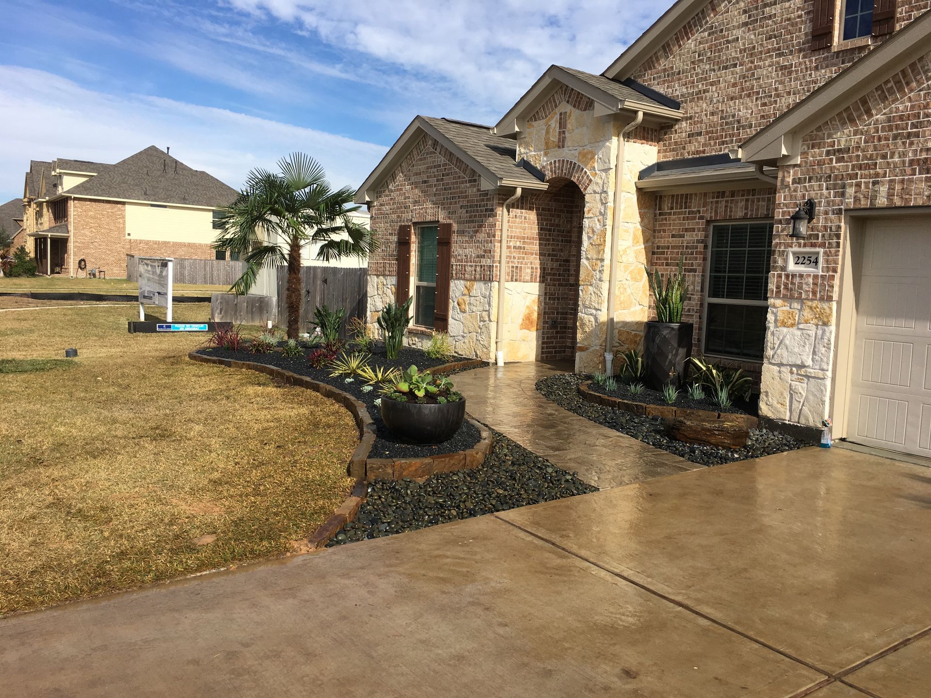 Suburban homes with stone facades, wet driveway, and a dry landscaped front yard after rain