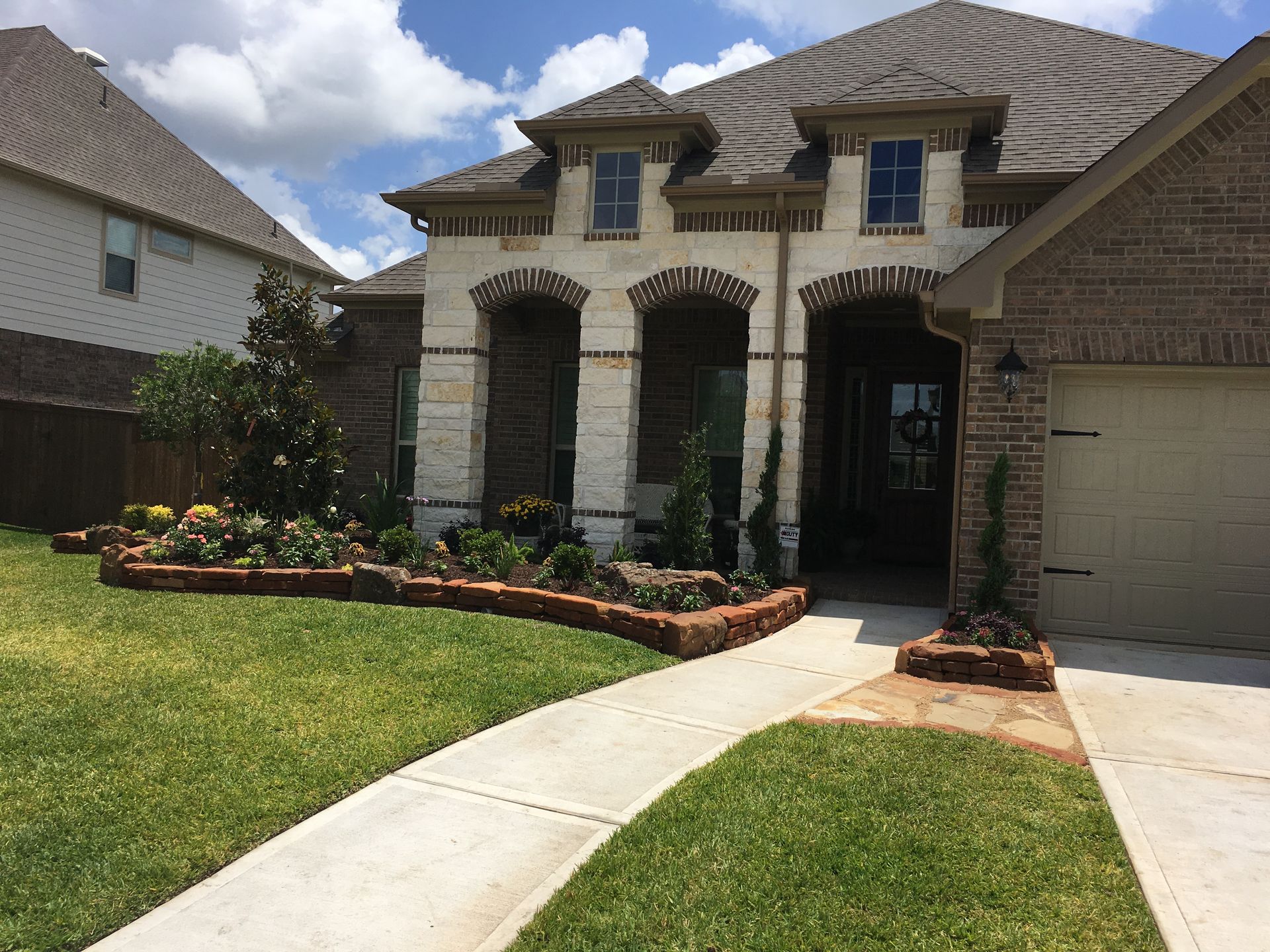 Suburban brick house with arched entry, garage, and manicured lawn under cloudy sky